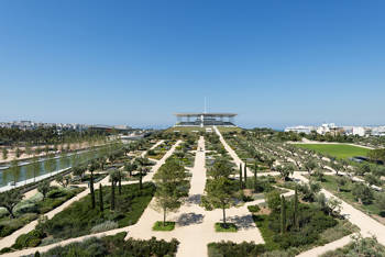 Photo showing a large garden with trees and an elongated pond that ends in a large glass building